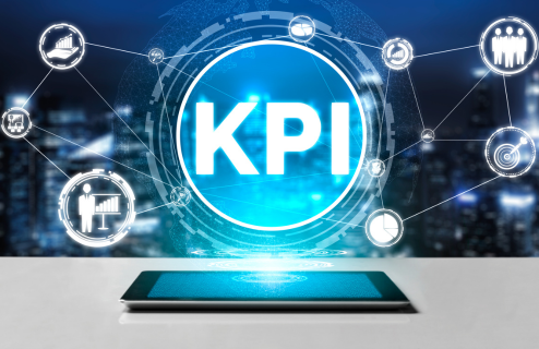 Grafika przedstawiająca kluczowy wskaźniki efektywności – wykresy, ikony i napis 'KPI' nad tabletem.